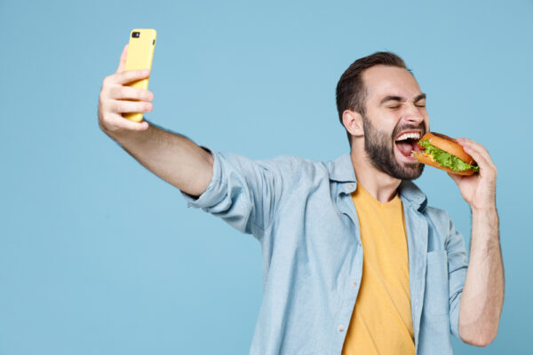 man eating hamburger while taking selfie